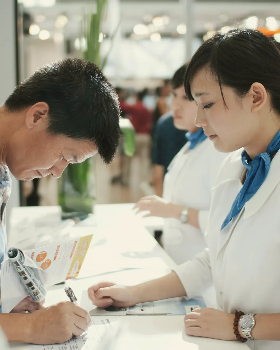 A registration host helps a guest sign in at an event desk.