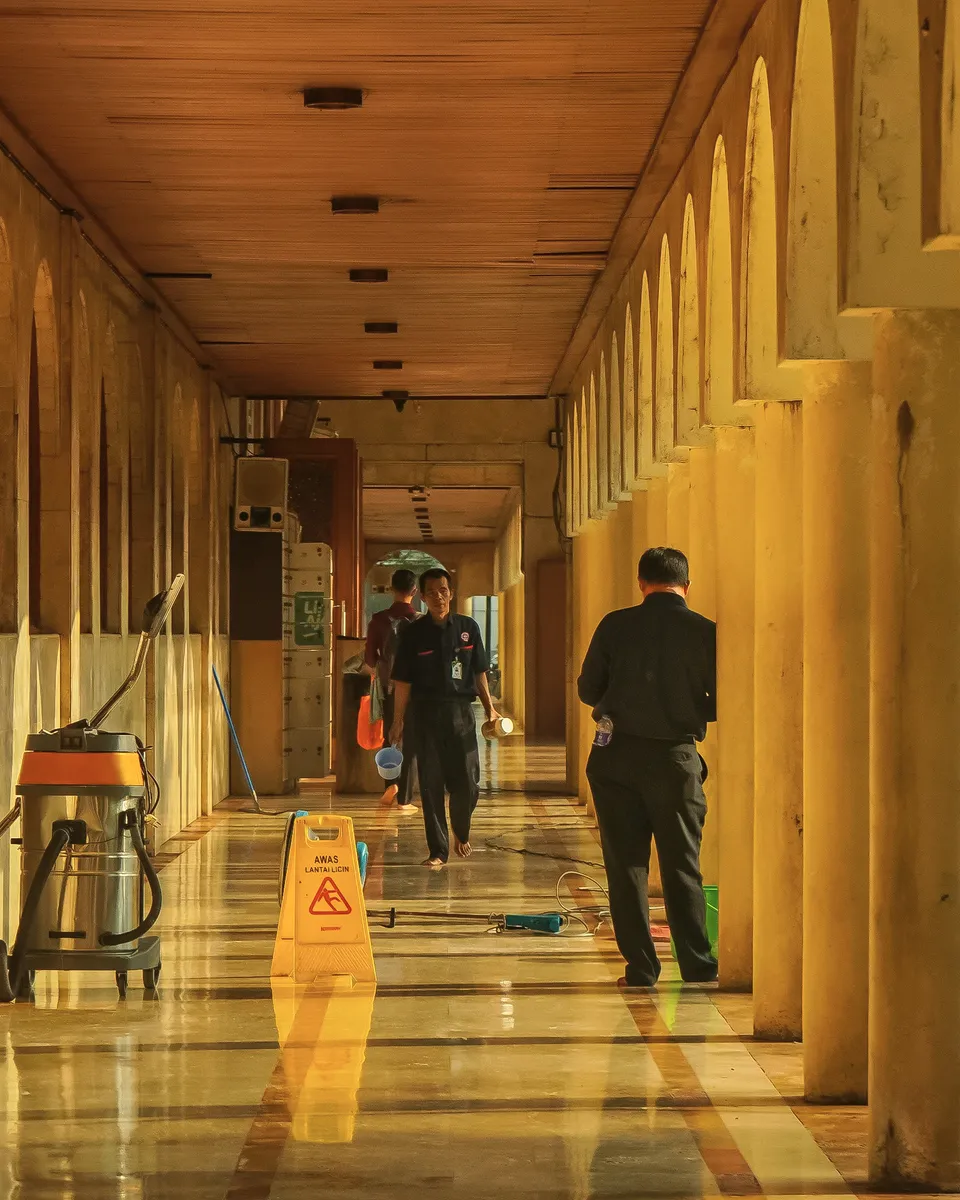 A cleaning crew at work in a long, sunlit colonnade.