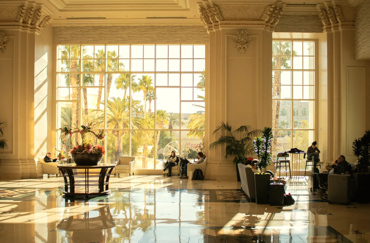 A bright hotel lobby with palms beyond tall windows.